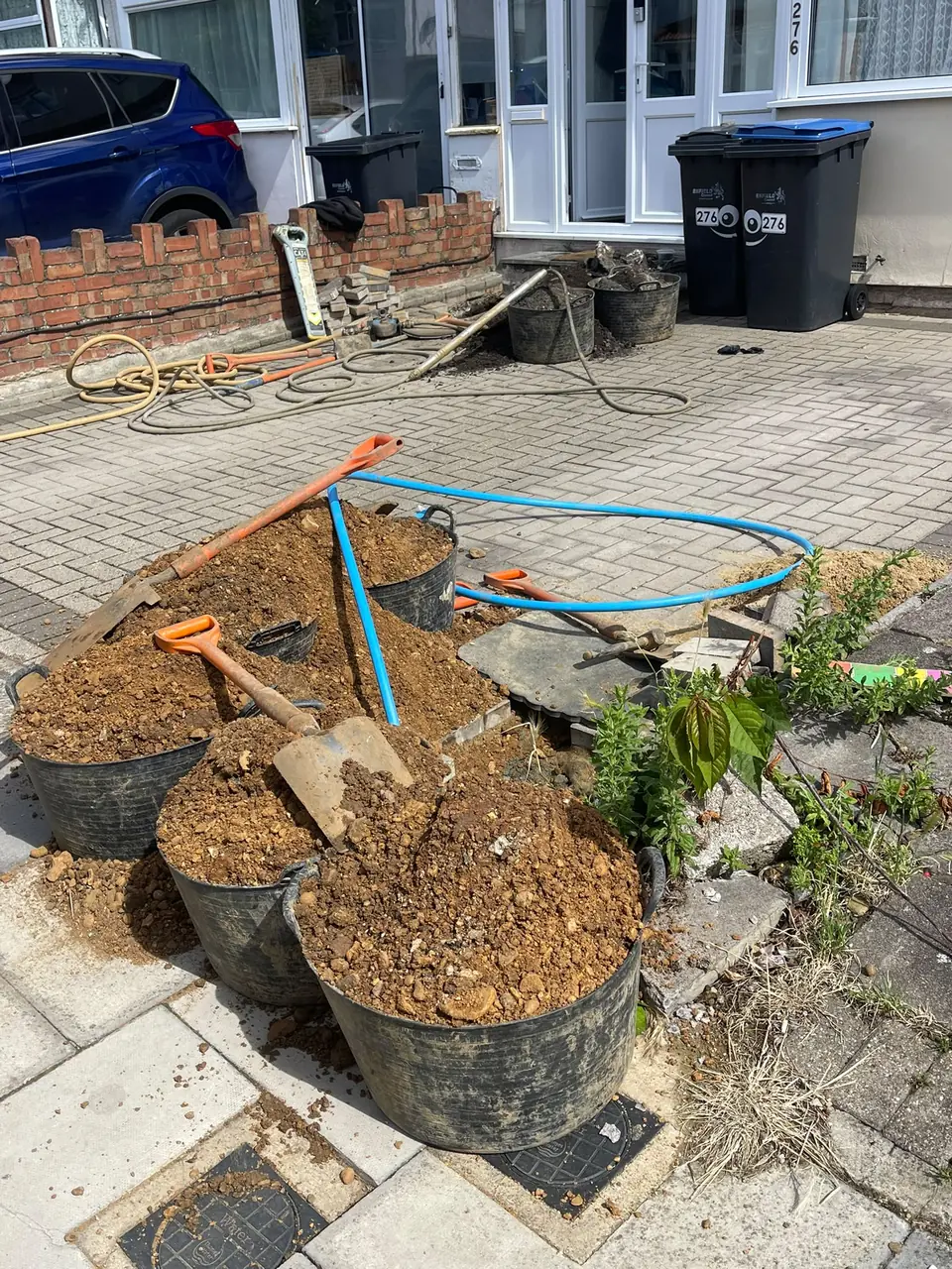 Compact excavation with blue water pipe on a residential driveway